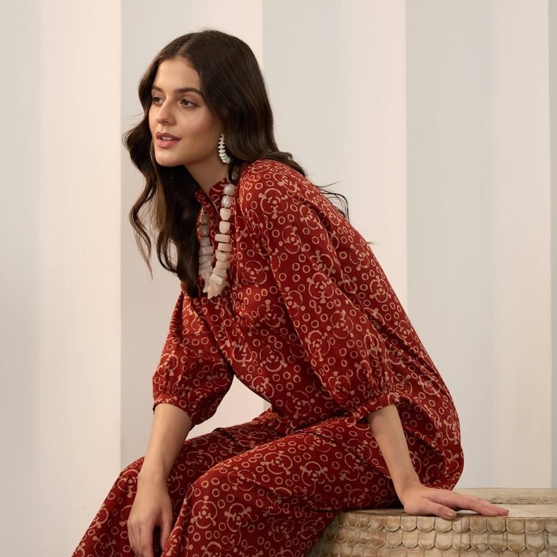 A woman in a patterned red outfit and statement necklace.